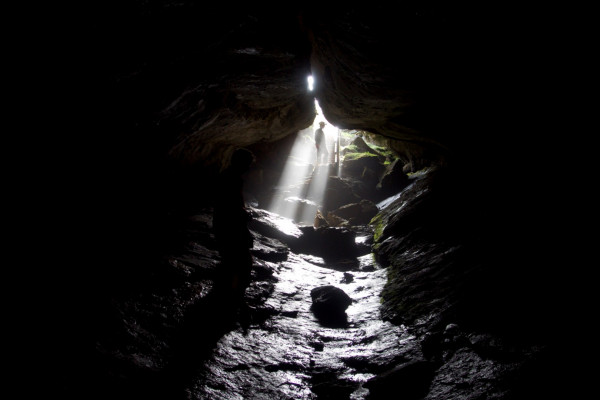 a person in a shaft of light in a cave entrance