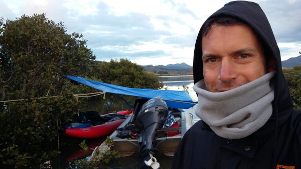 a scientist in front of a boat loaded with instruments and a mangrove bay in the background