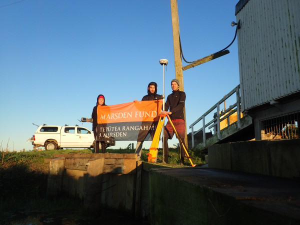 Three researchers hold up a flag in evening light