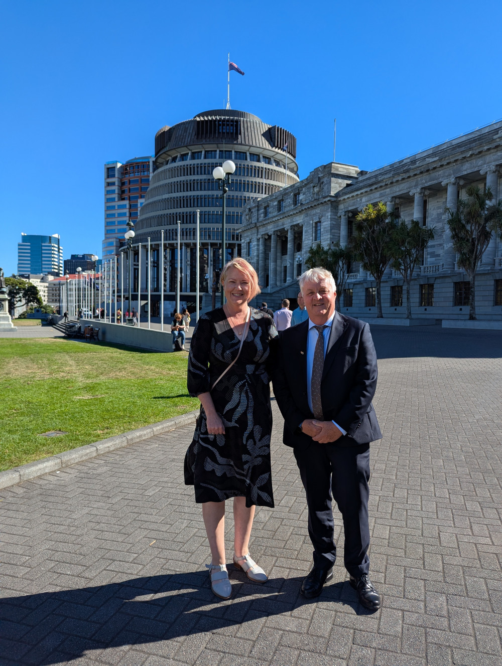 Dr Sara Edwards and Prof Andrew Allan stand in bright sunshine, in formal attire in front of the Beehive